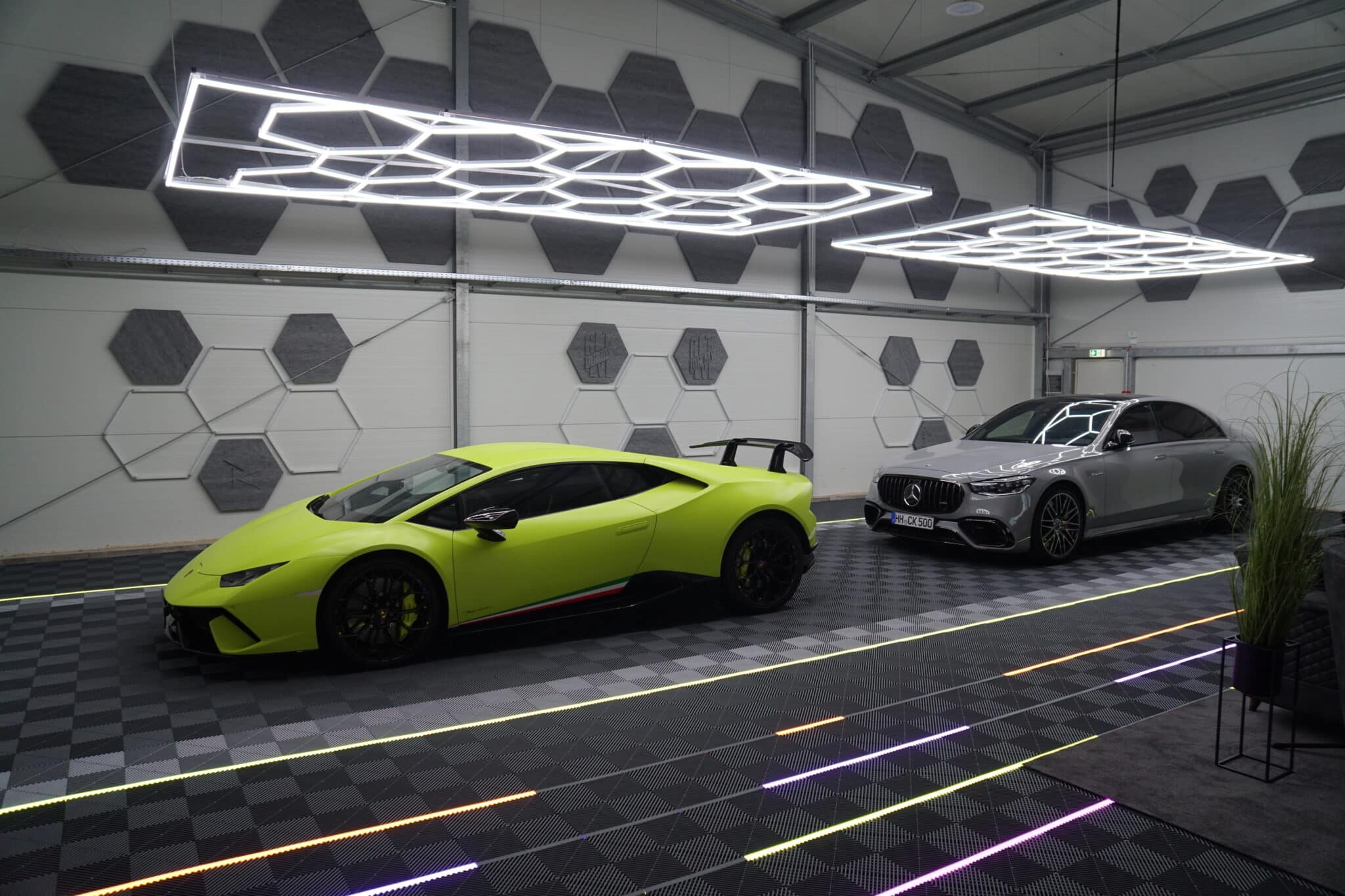Exklusive Fahrzeughalle mit schwarzem Klickfliesenboden, LED-Lichtdesign und zwei Luxusfahrzeugen – einem gelben Lamborghini und einem silbernen Mercedes-AMG