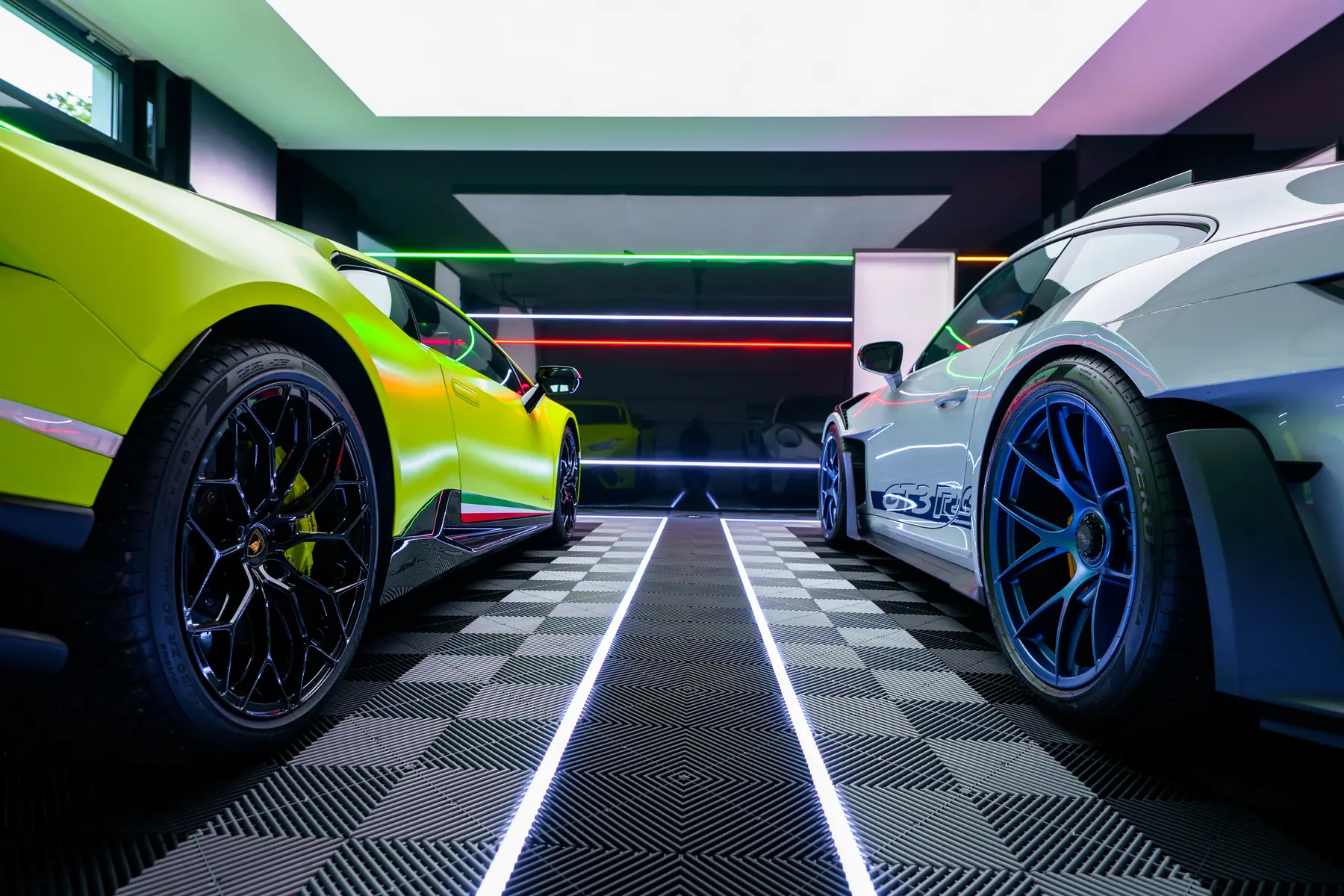 Lamborghini Huracán und Porsche 911 GT3 RS auf Klickfliesen, tiefe Perspektive auf Fahrgasse und LED-Linien