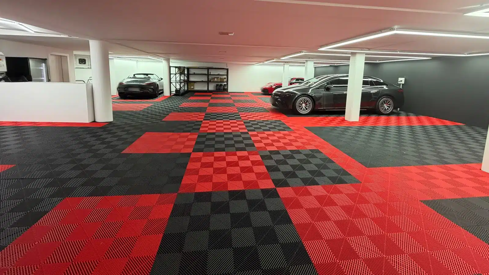 Große Tiefgarage mit Performance-Floor-Klickfliesen in Rot und Schwarz mit Karomuster, Säulen und mehreren Fahrzeugen